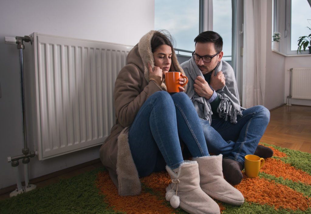 Couple sitting in front of furnace with blankets on